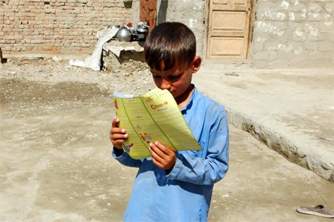 アフガニスタン：新型コロナウイルスの感染予防啓発パンフレットを読む男の子