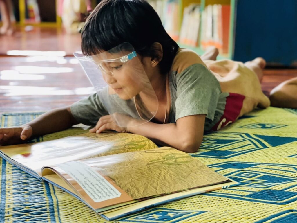 難民キャンプのコミュニティ図書館で絵本に夢中になる子ども。コロナ禍のためフェイスシールドを着用。