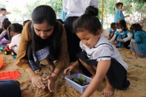 砂遊びをする女の子と教員