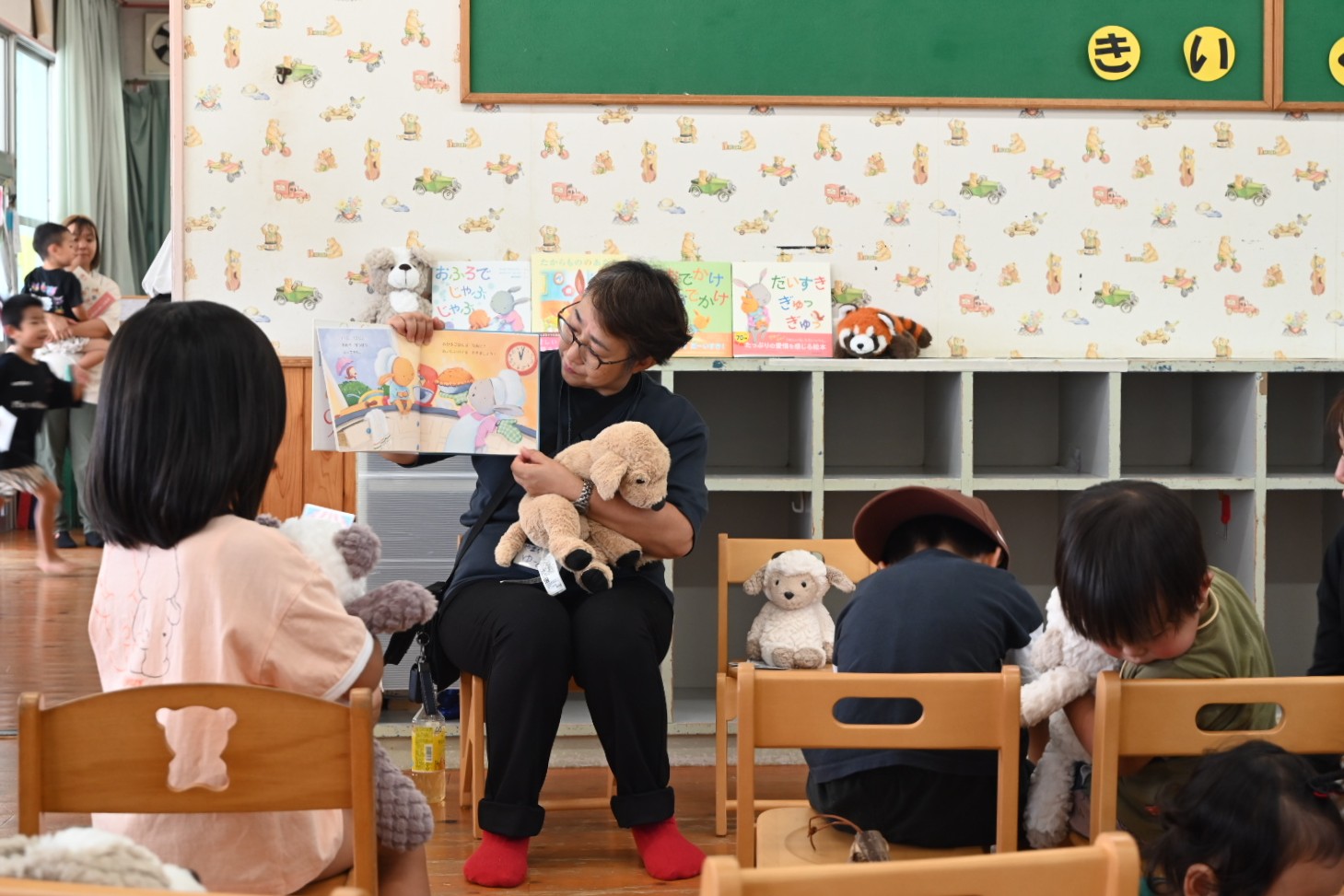 てとめっとのスタッフが、ぬいぐるみを持っている子どもたちの前で絵本の読み聞かせをしている様子
