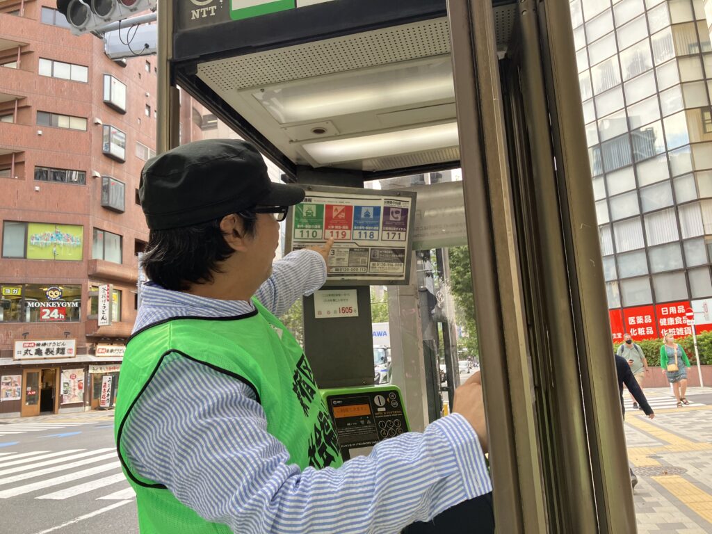 公衆電話内の非常時ダイアルを紹介している様子